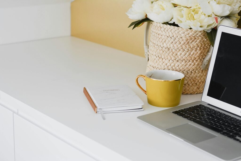 Elegant home workspace setup with a yellow mug, laptop, and flowers in a woven basket on a desk.